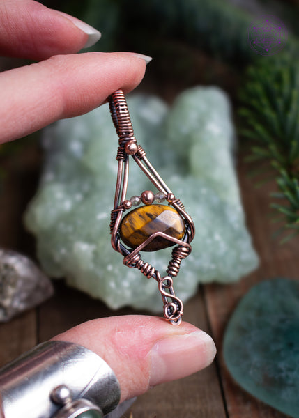 Tiger Eye copper wire wrapped pendant with a geometric design of an elongated diamond where the faceted tiger eye stone sits between the two side corners. The pendant comes to a point with an S curve around the point like roots going into the ground. This pendant is like a bare tree in winter with the golden citrine accent beads like the last leaves hanging on. Held in hand to show the facets and golden flashes of the crystals.
