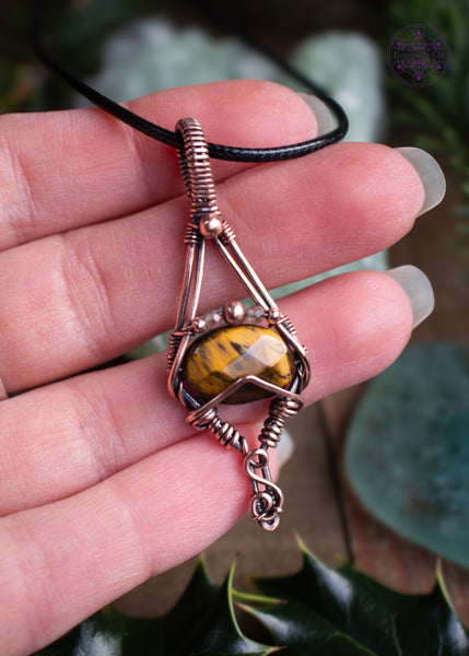 Tiger Eye copper wire wrapped pendant with a geometric design of an elongated diamond with a faceted golden tiger eye crystal and citrine and copper beads over the tiger eye. simple and elegant, held in hand to show size reference.
