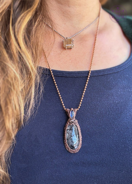 an oval cut black tourmaline quartz crystal wrapped with copper wire like a basket weave and a blue kyanite and smoky quartz accent crystals in the bail. Shown being worn to show where it hangs on the neckline.