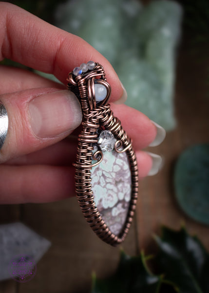 Copper wire wrapped Variscite pendant with accent stones of diamond quartz and moonstone made to look like a winter goddess, named Chione after the greek goddess of snow. Shown held in hand and looking at the top left to show the details and flash of the moonstone crown at the top of the bail.