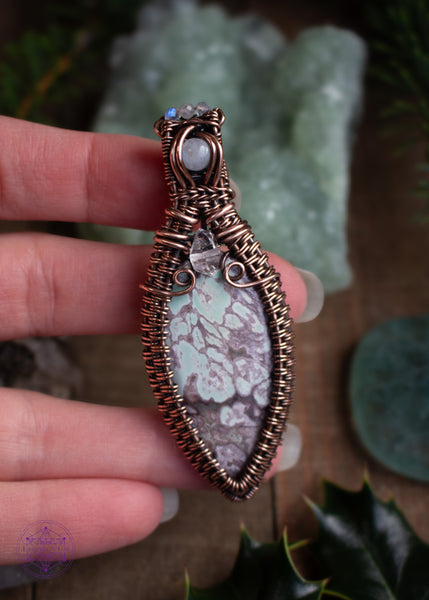 Copper wire wrapped Variscite pendant with accent stones of diamond quartz and moonstone made to look like a winter goddess, named Chione after the greek goddess of snow. Shown held in hand with the moonstone flashing blue in the light.