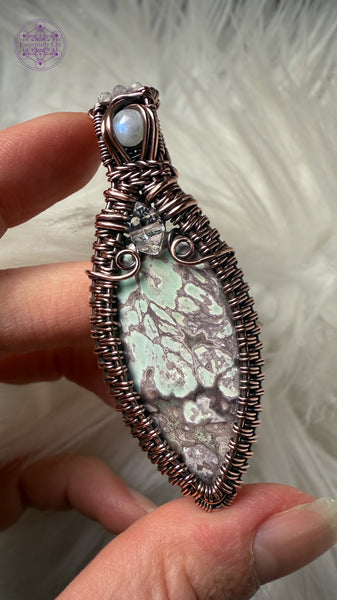 Copper wire wrapped Variscite pendant with accent stones of diamond quartz and moonstone made to look like a winter goddess, named Chione after the greek goddess of snow. Shown held in hand with a white faux fur for contrast.
