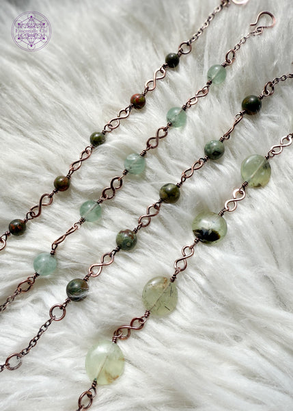 Picture is of 4 different bracelets with the figure 8 links in different stones laying on a white faux fur blanket.