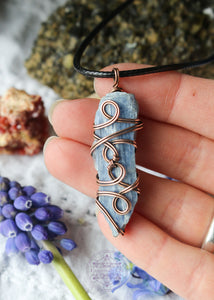 This copper wire wrapped pendant shown in hand for size reference has 4 swirls along the face of the blue kyanite and is connecting the two middle swirls together. Raw Blue Kyanite Wire Wrapped Necklace for energy protection, featuring a simple, everyday wear design that enhances communication, alignment, tranquility, restful sleep, and dream recall.