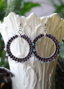 Dark Witch Beaded Hoop Earrings featuring a matte black, pomegranate red, hematite, and chalcedony-colored seed bead pattern. Suspended from sterling silver ear hooks, these 2.5-inch earrings exude enchanting allure