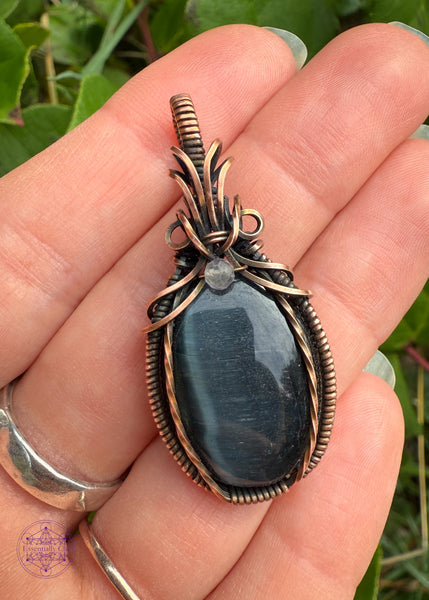 Beautiful Blue Tigers eye pendant with a bail shaped like a pineapple like top and a dark topaz crystal holding them together. The front of the pendant has two twisted wires going up the side. Simple and elegant. Held in hand to show size reference.