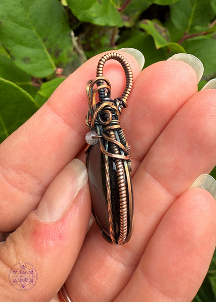 Beautiful Blue Tigers eye pendant with a bail shaped like a pineapple like top and a dark topaz crystal holding them together. The front of the pendant has two twisted wires going up the side. Simple and elegant. Held showing the side details and how thin it is for a lightweight design.