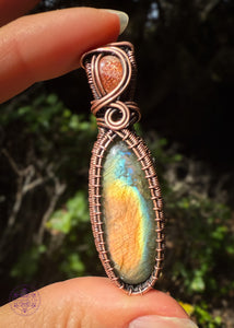 Picture of the two stone pendant with labradorite in colors of mainly orange then thin bands of yellow, blue and green as the main stone and in the bail is a lattice sunstone with sparkling flashes as the copper swirls around it. An elegant wrap and flashy at the same time. Held in the sun for full flash. 