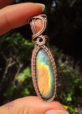 Picture of the two stone pendant with labradorite in colors of mainly orange then thin bands of yellow, blue and green as the main stone and in the bail is a lattice sunstone with sparkling flashes as the copper swirls around it. An elegant wrap and flashy at the same time. Held in the sun for full flash. 