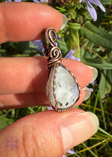 Beautiful Rainforest moonstone teardrop pendant wrapped in copper wire is a dainty small crystal pendant. The front square wires are twisted over the edge of the crystal and the bail has a few elegant swoops. Showing the side view to see the depth of the crystal.