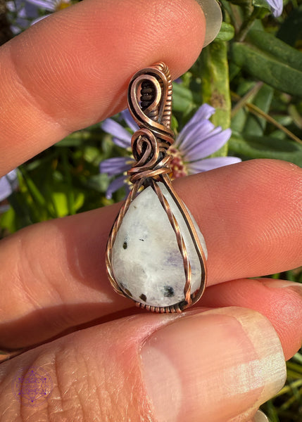Beautiful Rainforest moonstone teardrop pendant wrapped in copper wire is a dainty small crystal pendant. The front square wires are twisted over the edge of the crystal and the bail has a few elegant swoops. Showing the side view to see the depth of the crystal.