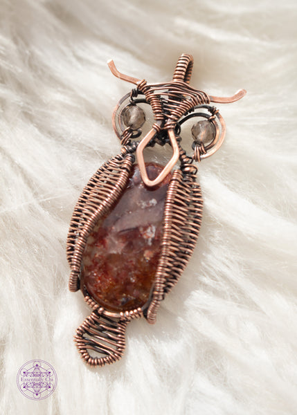 copper wire wrapped great horned owl pendant with a fire quartz belly, wire woven wings, and smoky quartz eyes sitting on a white faux fur background.