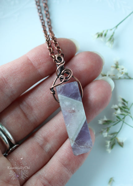 Immerse yourself in the energy of our Freya Chevron Amethyst Copper Wire Wrapped Pendant. Named after the Norse goddess of love and beauty, this piece enhances intuition, promotes emotional healing, and reduces stress, aligning your energy for a harmonious existence. This chevron amethyst has a big V section of quartz in the middle and purple banding on the top and bottom.
