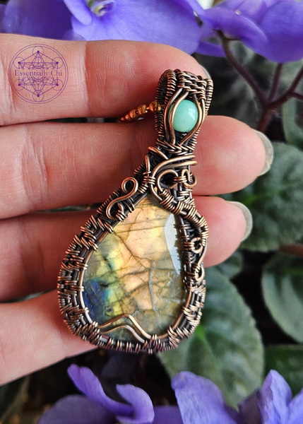 Golden orange and blue flash labradorite in a teardrop shape, with a woven frame and a swirl design on both sides. An aqua green chrysoprase crystal in the bail. 