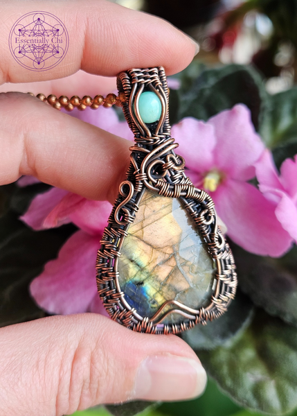 Golden orange and blue flash labradorite in a teardrop shape, with a woven frame and a swirl design on both sides. An aqua green chrysoprase crystal in the bail. 