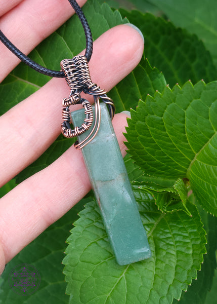 green aventurine pendant wrapped with copper wire and a black cotton waxed cord. The crystal is a rectangle and the copper wrapping is close to the bail showing more of the stone. Shown in hand for size reference. 