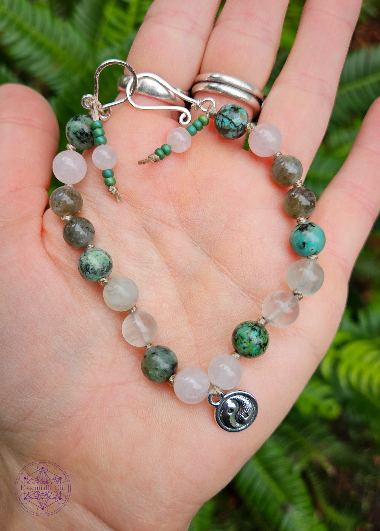 Hand-knotted beaded boho bracelet in a pastel pink and green theme. This bracelet has a silver plated yin yang charm in the center. Beads are knotted with a sand colored nylon thread with crystals such as rose quartz, African turquoise, green fluorite, and labradorite. Clasp is a silver plated hook closure.