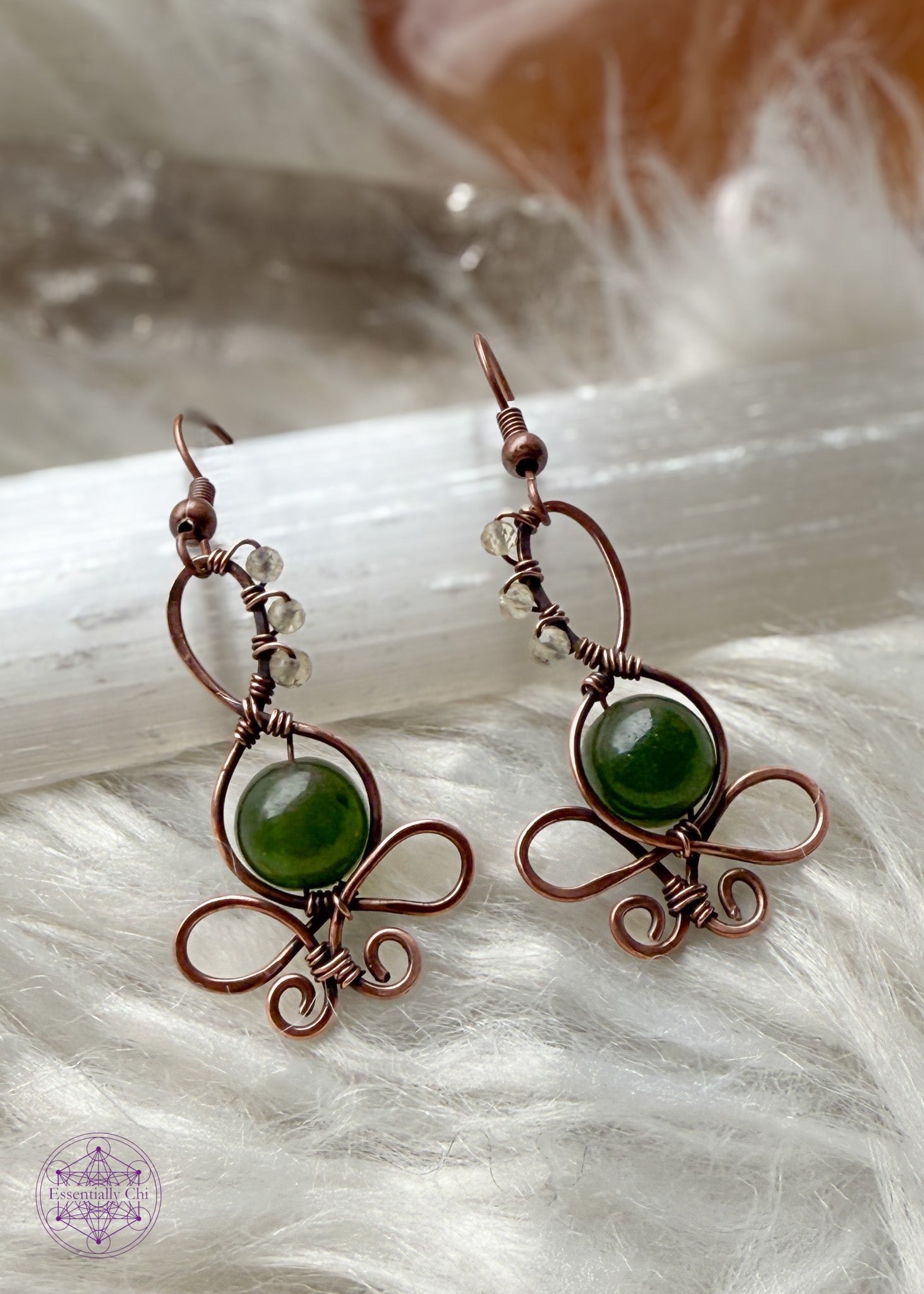 These earth goddess earrings have a green jade crystal belly and small faceted crystal beads along her head. Sitting on a selenite crystal on white faux fur.