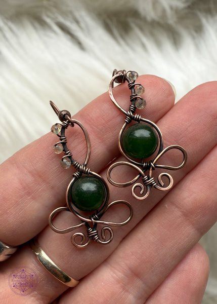 These earth goddess earrings have a green jade crystal belly and small faceted crystal beads along her head. Wrapped in copper wire and hung from ear hooks. Held in hand to show size reference.