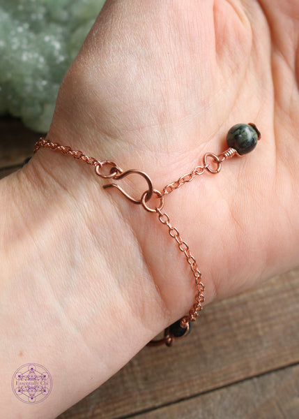 Twisted copper wire wrapped bracelet features Kambaba beads. Showing the backside of bracelet on wrist to see hook clasp and beaded extension chain and Kambaba Jasper charm that you can hold onto to secure the clasp.