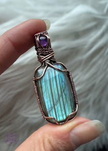gorgeous blue flash labradorite with dark vertical streaks through it is wrapped in copper wire and held at the corners so it didn't cover the flashy parts. The bail is a woven pattern and a small dark purple amethyst stone to add to the depths of this pendant. 