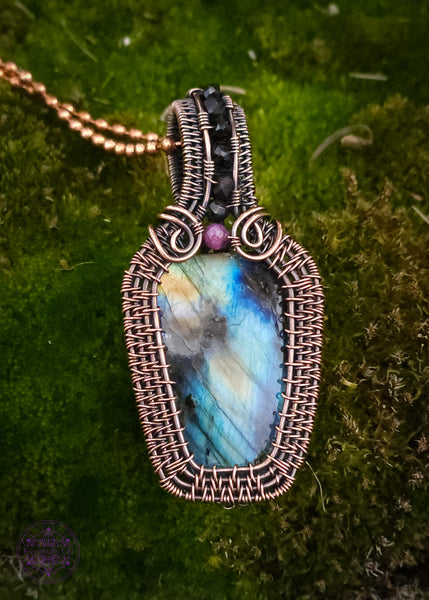 Copper wire wrapped labradorite coffin pendant with a red tourmaline accent stone at the top of the coffin to symbolize blood color, and then black spinel beads along the center of the bail. nice thick wrap style to create the ultimate statement piece. Labradorite has mainly blue flash with a few dark spots and yellow to orange colors. 