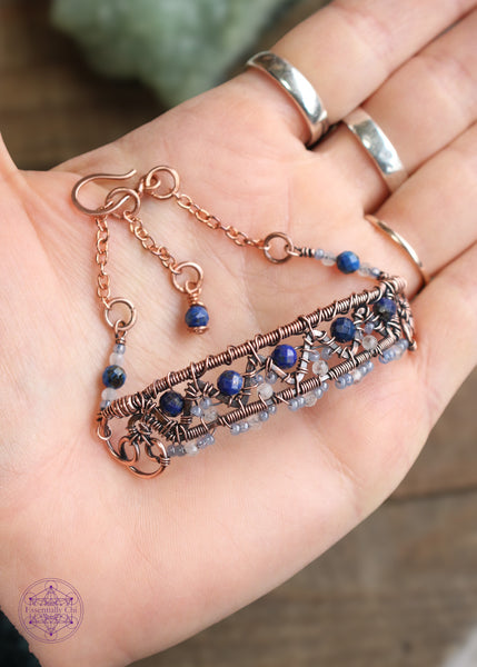 Copper wire wrapped bracelet features faceted lapis lazuli and moonstone woven between a zig zag design and added smoky blue seed beads for a filagree look. This view shows the front of the bracelet and the billow curls on the side as connector loops and the extension beaded detail of lapis lazuli, moonstone and seed bead combo. Bracelet is laying in the palm of my hand to help show contrast between the bead colors and my skin tone.