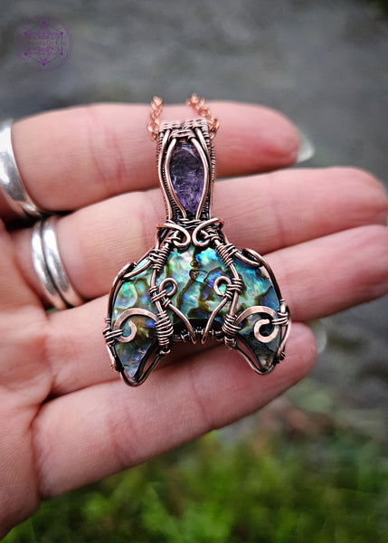 Abalone and Amethyst mermaid tail pendant wrapped in copper wire filagree design. The fin is an Abalone moon and the amethyst is faceted like the scales on the mermaid tail. Shown in hand for size reference.
