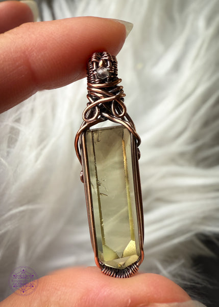 Copper wire wrapped Natural Citrine point pendant with a small smoky quartz bead in the bail. Held in fingers with a white faux fur background to show the details inside the crystal. There are two phantoms at the top of the crystal and the wrap doesn't cover any of the crystal to allow light to shine through the back.