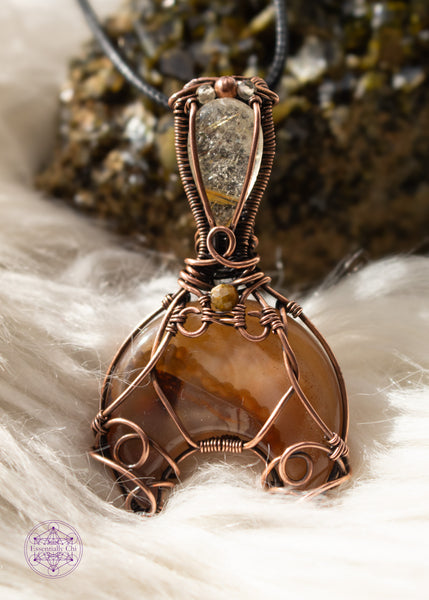 Copper wire wrapped Whale Tail or Mermaid Tail necklace with the fin in a natural agate with cascading colors of chocolate brown to caramel and butterscotch. The tail has swirls at the base to secure the stone in, and at the base of the bail is a natural colored tourmaline that matches the agate. The bail has a golden rutile upside-down tear drop and on top of that is a copper and two citrine beads. Shown on a white faux fur background leaning against an epidote cluster.