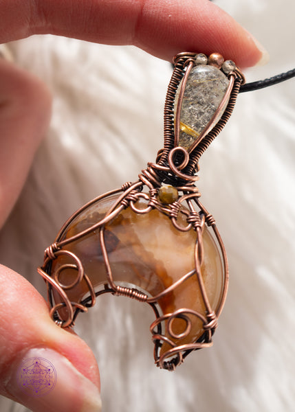  Copper wire wrapped Whale Tail or Mermaid Tail necklace with the fin in a natural agate with cascading colors of chocolate brown to caramel and butterscotch. The tail has swirls at the base to secure the stone in, and at the base of the bail is a natural colored tourmaline that matches the agate. The bail has a golden rutile upside-down tear drop and on top of that is a copper and two citrine beads. Shown on a white faux fur background held in hand for size reference.
