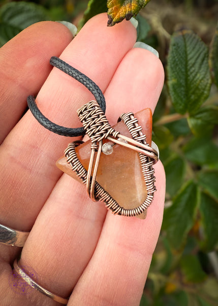 Small arrow shaped orange aventurine crystal pendant wrapped in copper with a woven design and a citrine crystal at the base of the bail. Held in hand showing the size reference, the length of the upper part of my pinky.