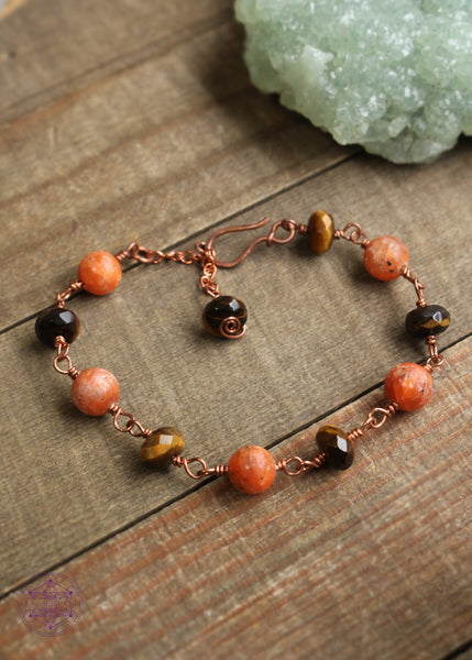 Copper wire wrapped bracelet features 8mm Orchid Calcite beads individually wrapped with faceted rondelle Tiger Eye beads individually wrapped linking together for an elegant bracelet. Shown on  wooden board to show the whole bracelet with clasp. The Tiger Eye Charm at the end has a small swirl design.