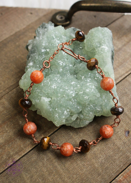 Copper wire wrapped bracelet features 8mm Orchid Calcite beads individually wrapped with faceted rondelle Tiger Eye beads individually wrapped linking together for an elegant bracelet. Shown on green crystal laying on a wooden board to show the whole bracelet with clasp.