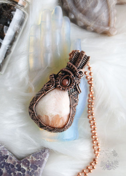 Elevate your spiritual style with our Peach Scolecite Copper Wire Wrapped Necklace. Delicately woven copper embraces a teardrop-shaped peach scolecite, accompanied by a pink jasper in the bail. This handcrafted masterpiece exudes calming energy, promoting emotional healing and spiritual upliftment. Perfect for Libra & Capricorn zodiacs, this necklace aligns with the crown and third eye chakras, fostering a sense of tranquility and connecting you to the divine feminine energy.