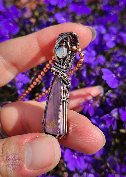 Copper wire wrapped Phosphosiderite crystal with a flashy moonstone accent crystal in the bail. The Phosphosiderite is a lavender colored crystal with some beige inclusions throughout in a thin tall triangle shape, wrapped to show off as much as the crystal as possible and in an elegant design.