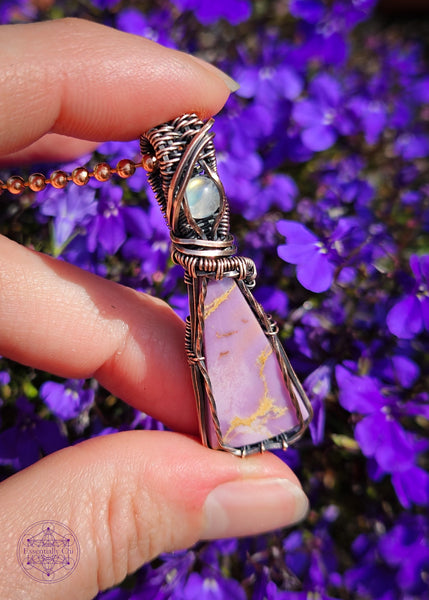 Copper wire wrapped Phosphosiderite crystal with a flashy moonstone accent crystal in the bail. The Phosphosiderite is a lavender colored crystal with some beige inclusions throughout in a thin tall triangle shape, wrapped to show off as much as the crystal as possible and in an elegant design.