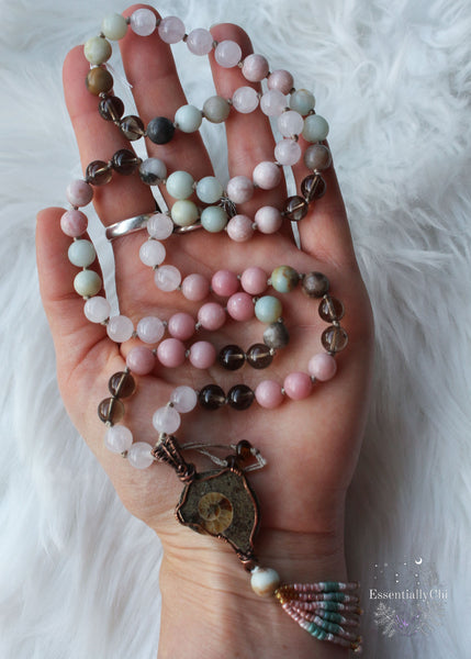 This mala is 72 beads that slip easily over the head and short enough where the pendant sits around the heart space. The pendant is a copper wire wrapped ammonite with a beaded beaded tassel. Mala beads include rose quartz for self love, smoky quartz for protection and positivity, pink sandstone for helping you stand strong in the midst of change, and amazonite for comfort in transition. Ammonite helps with stability in the midst of trauma.