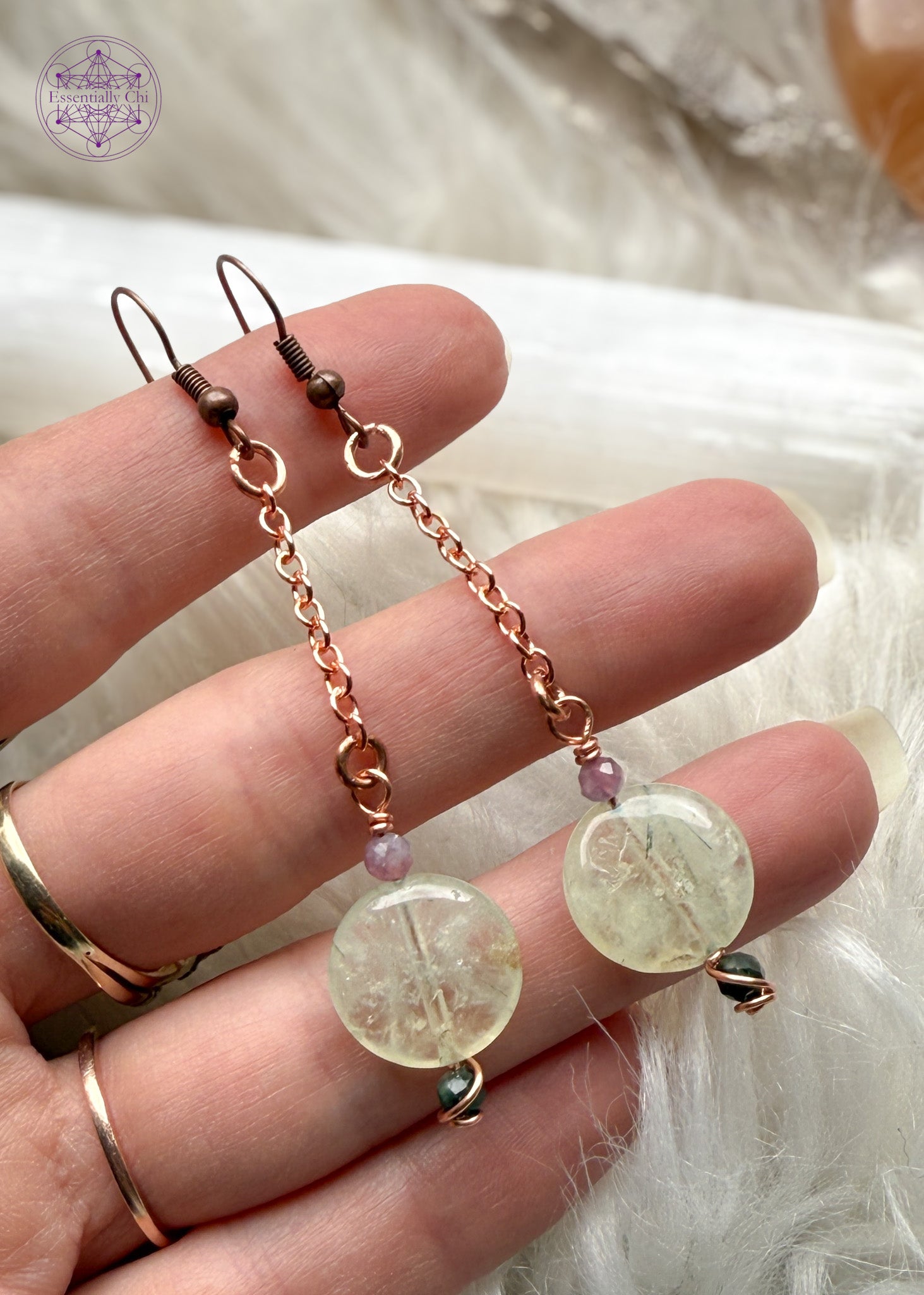 Gorgeous glowing prehnite dangle earrings hang from a long copper chain with green and pink tourmaline faceted beads and copper wire swirled around them. Hung on brass ear hooks gives them a total length of 3". Held in hand to show size reference.