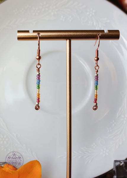 Pride Rainbow Earrings with seed bead drop design in rainbow pattern of purple to red on copper wire hanging 1.75" from rose gold-toned ear wires.