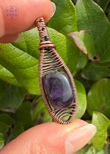 Purple Fluorite copper wire wrapped pendant in a simple minimal design. A snowshoe like shape with a deep purple rectangle bead in the center. Held in hand to show size. 