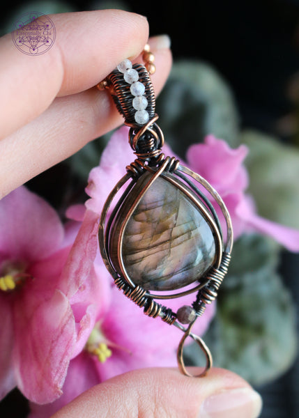 purple, orange, and blue green flash labradorite in a teardrop shape with a simple bail and 2mm moonstone faceted beads along the center of the bail. the bottom has a 3mm watermelon tourmaline attached as an accent stone.