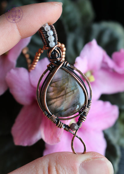 purple, orange, and blue green flash labradorite in a teardrop shape with a simple bail and 2mm moonstone faceted beads along the center of the bail. the bottom has a 3mm watermelon tourmaline attached as an accent stone.