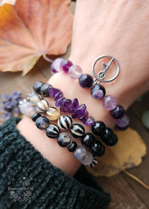 A collection of Energy Protection Stretch Bracelets crafted with various crystals. Bracelet 1 features Dragon Vein Agate, Tibetan Agate, and Black Onyx. Bracelet 2 includes Black Tourmaline and Tibetan Agate. Bracelet 3: Rainbow Obsidian and Amethyst chip crystals. Bracelet 4 showcases Purple Fluorite with a Yoga Tree Pose charm.