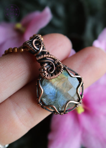 purple and orange flash labradorite in a circle shape secured with triangle prongs, and a swirl design over the bail.