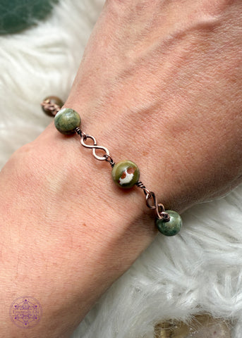 Copper wire wrapped bracelet features 8mm rainforest rhyolite beads individually wrapped with figure 8 Infinity links in-between for an elegant bracelet. Shown on wrist to see how it lays. 