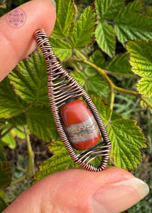 Copper wire wrapped red jasper bead with a river of quartz running in the middle of the jasper. Gorgeous bead centered in a minimalist design that kinda looks like a snow shoe. The bail is a simple criss cross woven design and the body of the pendant has a criss cross design centering the bead. held in hand for size reference.