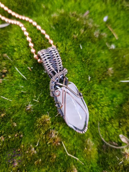 handcrafted filagree crystal necklace with a small rose quartz point wrapped in copper wire. Shown over green moss.