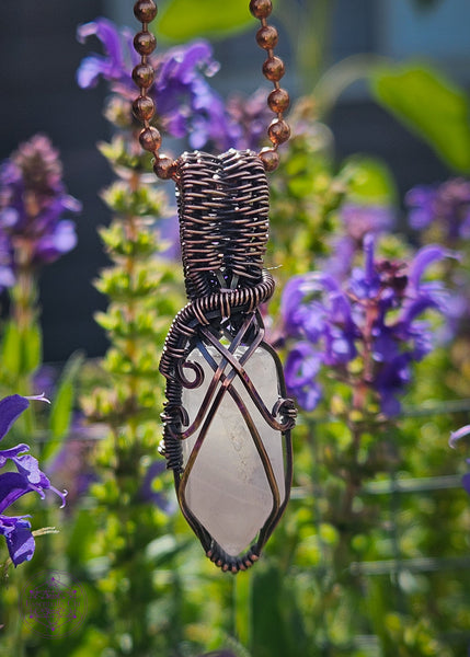 handcrafted filagree crystal necklace with a small rose quartz point wrapped in copper wire. Shown in front of Blue Sage flowers. 