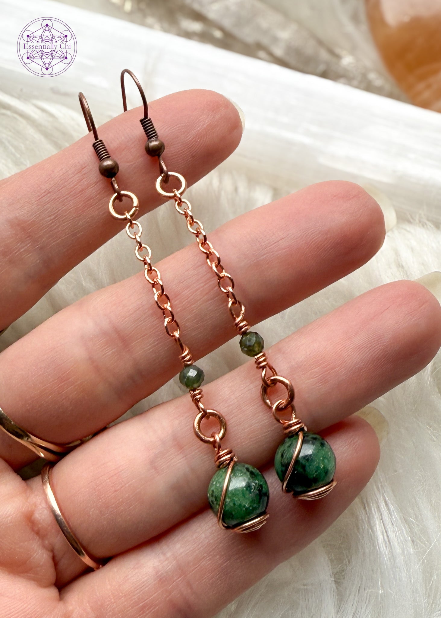 Gorgeous deep green Ruby Zoisite dangle earrings hang from a long copper chain and swirled in copper wire with green tourmaline faceted accent bead. Hung on brass ear hooks gives them a total length of 2.75". Held in hand to show size reference.